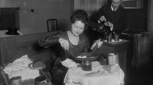 Schwarz-weiß Fotografie von 1920: Spiegeleier braten im Zimmer auf einem winzigen Spirituskocher.