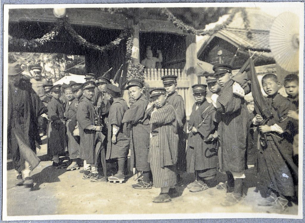 Fig. 2: A group of students waits in line to enter the exhibition of “visual arts and handicrafts” organized by the residents of Bandō POW camp. The exhibition was hosted by the nearby Ryōzenji temple, hence the statue in the center of the image. A no less imposing bearded German soldier is visible on the lefthand side of the photo. SBB-PK. Bandō-Sammlung H 57-07.