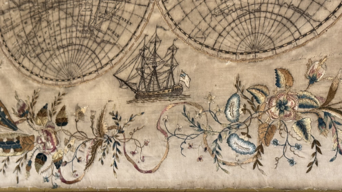 Detailaufnahme des Dreimaster Kriegsschiffes unterhalb der Erdhalbkugeln und dekorative Randverzierung aus gestickten Blättern, Blüten und Schleifenbändern