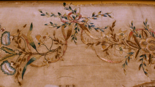 Detailaufnahme der dekorativen Elemente: obere Randverzierung aus gestickten Blättern, Blüten und Schleifenbändern